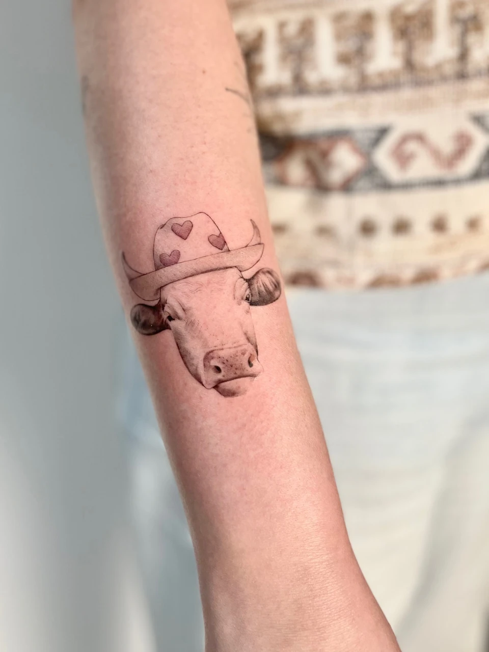 cow in a hat fine line tattoo on forearm