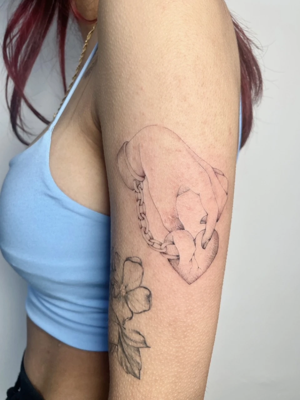 hand with a chain holding a heart
              fine line tattoo on arm